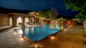 A swimming pool with a stone wall and arched openings, surrounded by stone tiles and benches.
