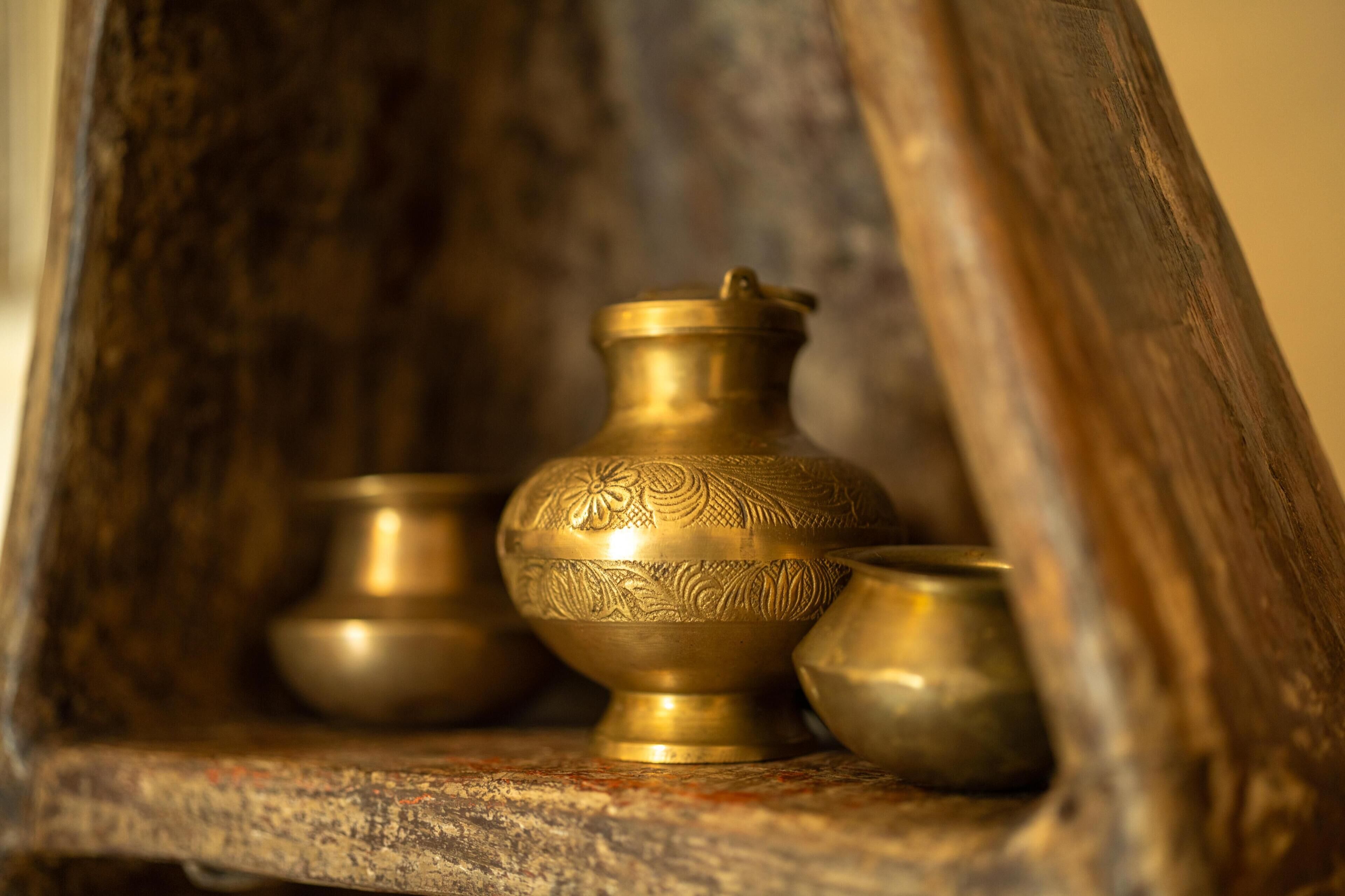 A wooden shelf with three brass bowls of varying sizes.