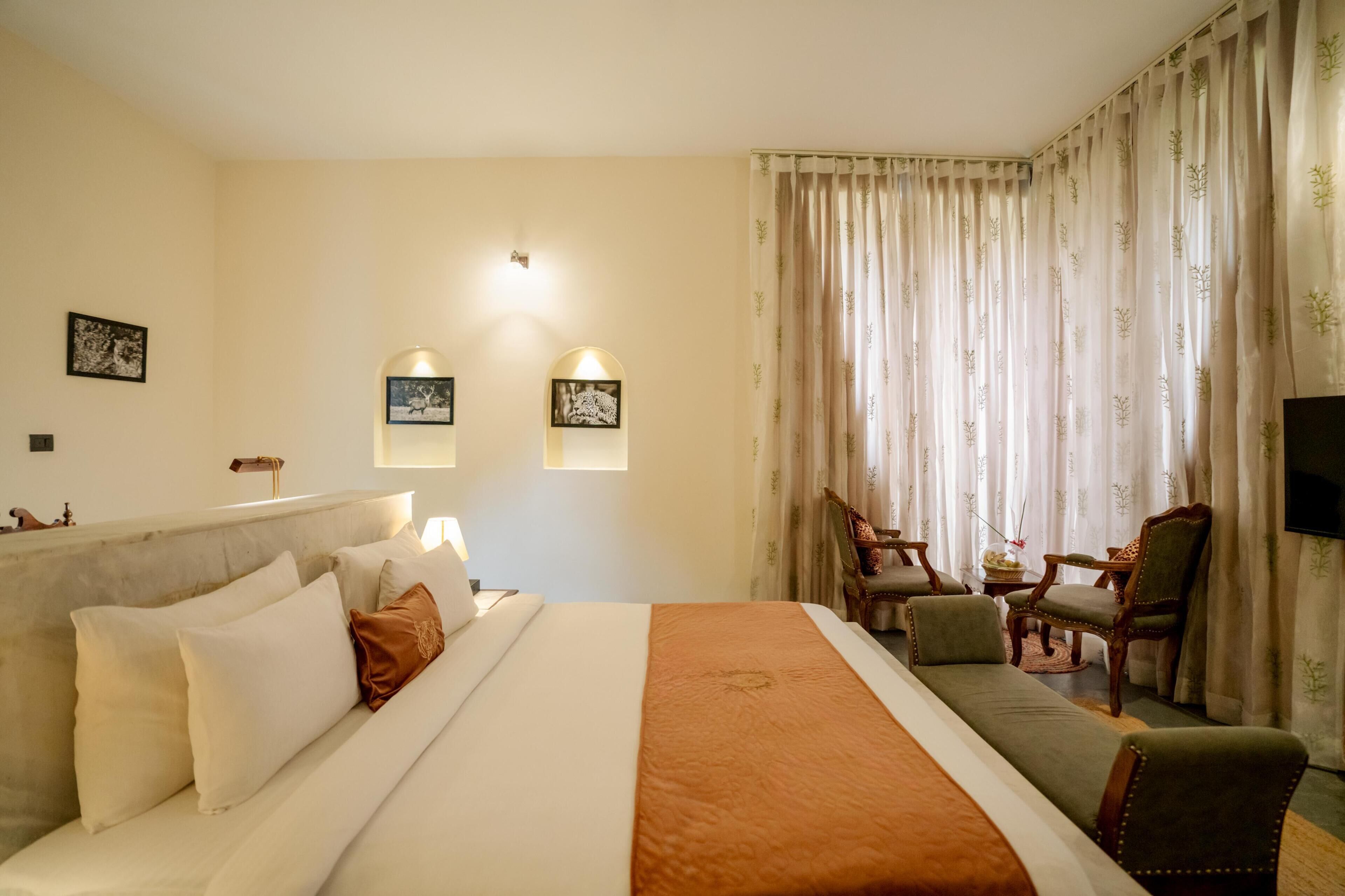 A hotel room with a large bed, a sofa, two armchairs, a small table, and a TV.