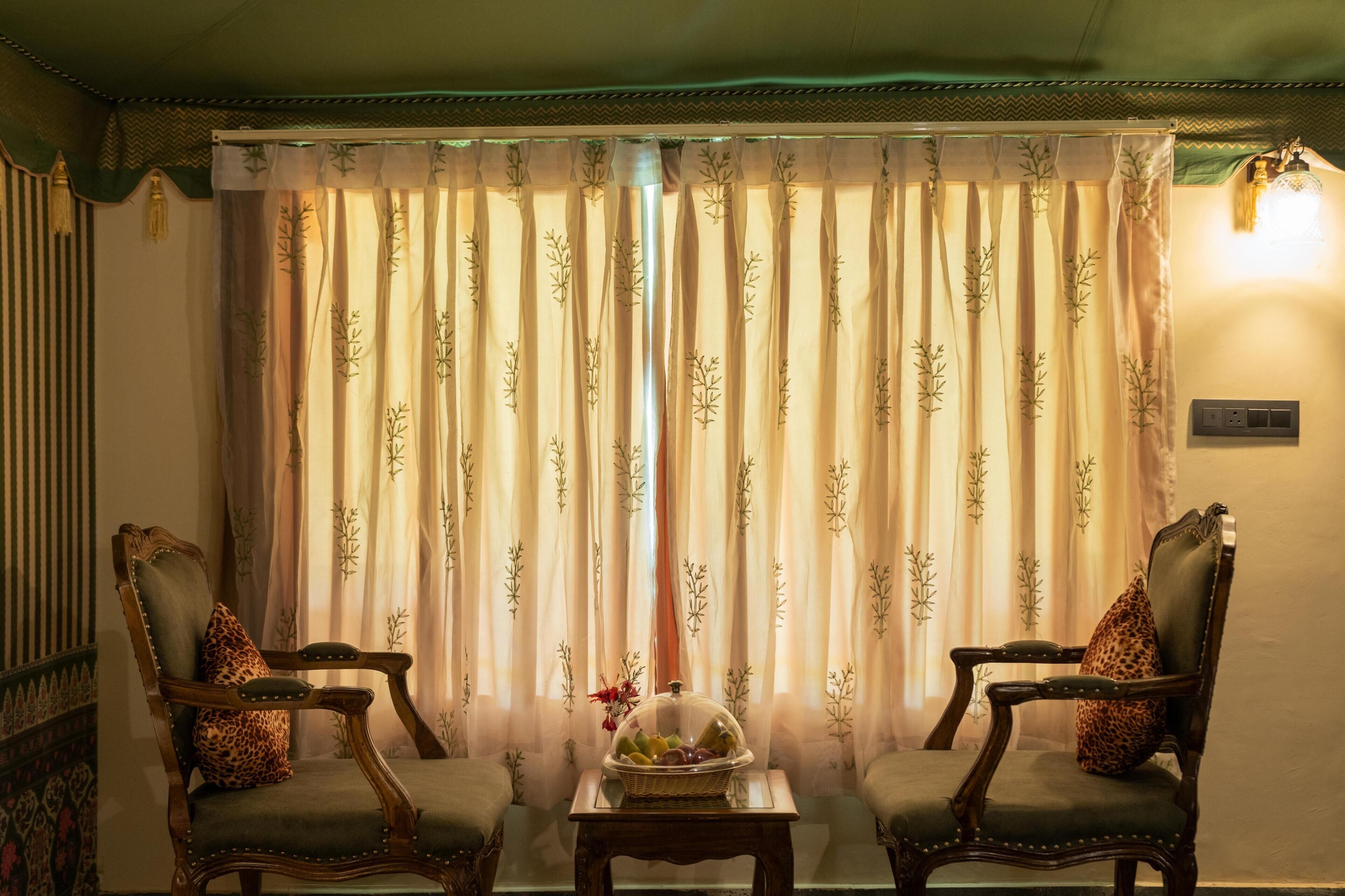 A room with two armchairs, a small table with a fruit basket, and a curtain with a leaf pattern.