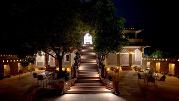 A staircase leading to a building entrance, surrounded by outdoor seating and potted plants.