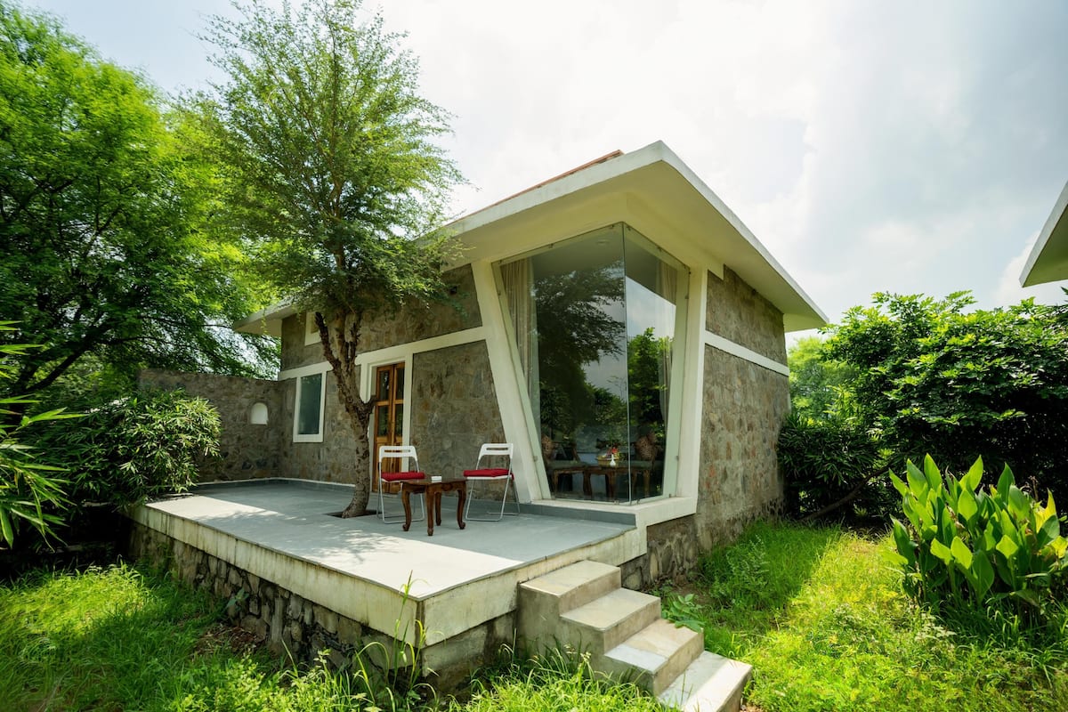 Een modern huis met een gevel van natuursteen, een glazen veranda en een klein terras met twee stoelen en een tafel.
