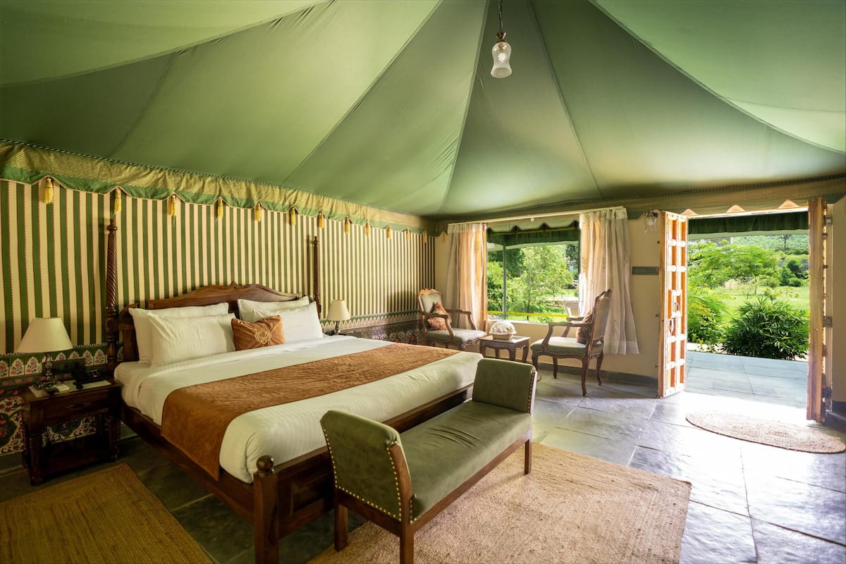 Een ruime tent met een groot bed, een bank en een tafel met stoelen.