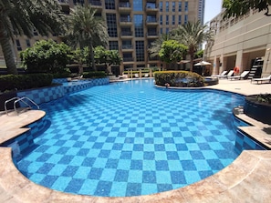 A swimming pool with a checkered pattern, surrounded by palm trees and a building with balconies. - Lux BnB I Standpoint Tower I Opera View (Dubai)