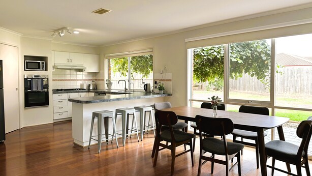 A modern kitchen with a central island, bar stools, and a dining table with chairs. - Close to Airport (Hillside)