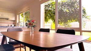 A dining area with a wooden table, four chairs, and a vase with flowers. - Close to Airport (Hillside)