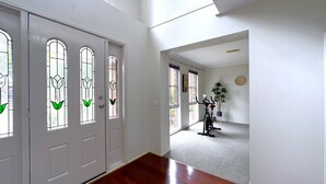 A hallway with white walls, a wooden floor, and a door with stained glass windows. - Close to Airport (Hillside)
