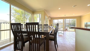 A dining area with a table and chairs, large windows, and a view of the backyard. - Open Range Zoo/Supper Comfortable Beds/Shopping Center (Point Cook)