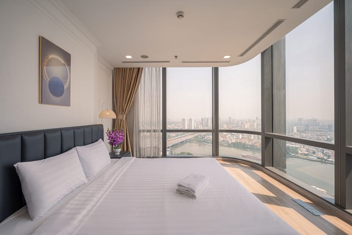 Una habitación de hotel moderna con una cama grande, vistas a la ciudad y un ventanal amplio.
