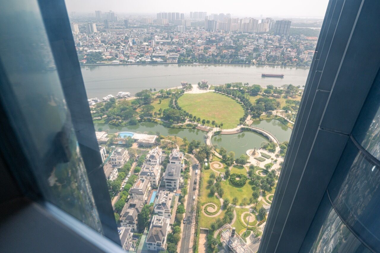 Um edifício alto com vista para o horizonte urbano, um rio e um parque com um gramado circular.
