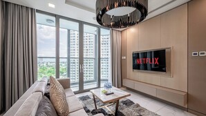 Una sala de estar moderna con un sofá, una mesa de centro, un televisor y vistas a un paisaje urbano a través de amplios ventanales.