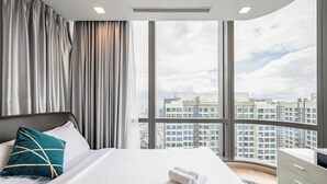 Una habitación de hotel moderna con una cama grande, vistas de la ciudad a través de ventanas de piso a techo y un horizonte urbano de fondo.