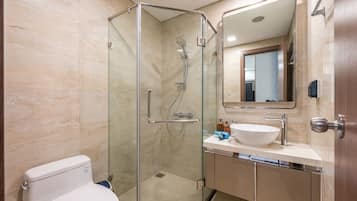 Un baño moderno con ducha de vidrio, inodoro blanco, lavamanos con espejo y paredes de azulejos color beige.