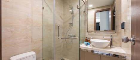 A modern bathroom with a glass-enclosed shower, a white toilet, a sink with a mirror, and beige tiled walls.