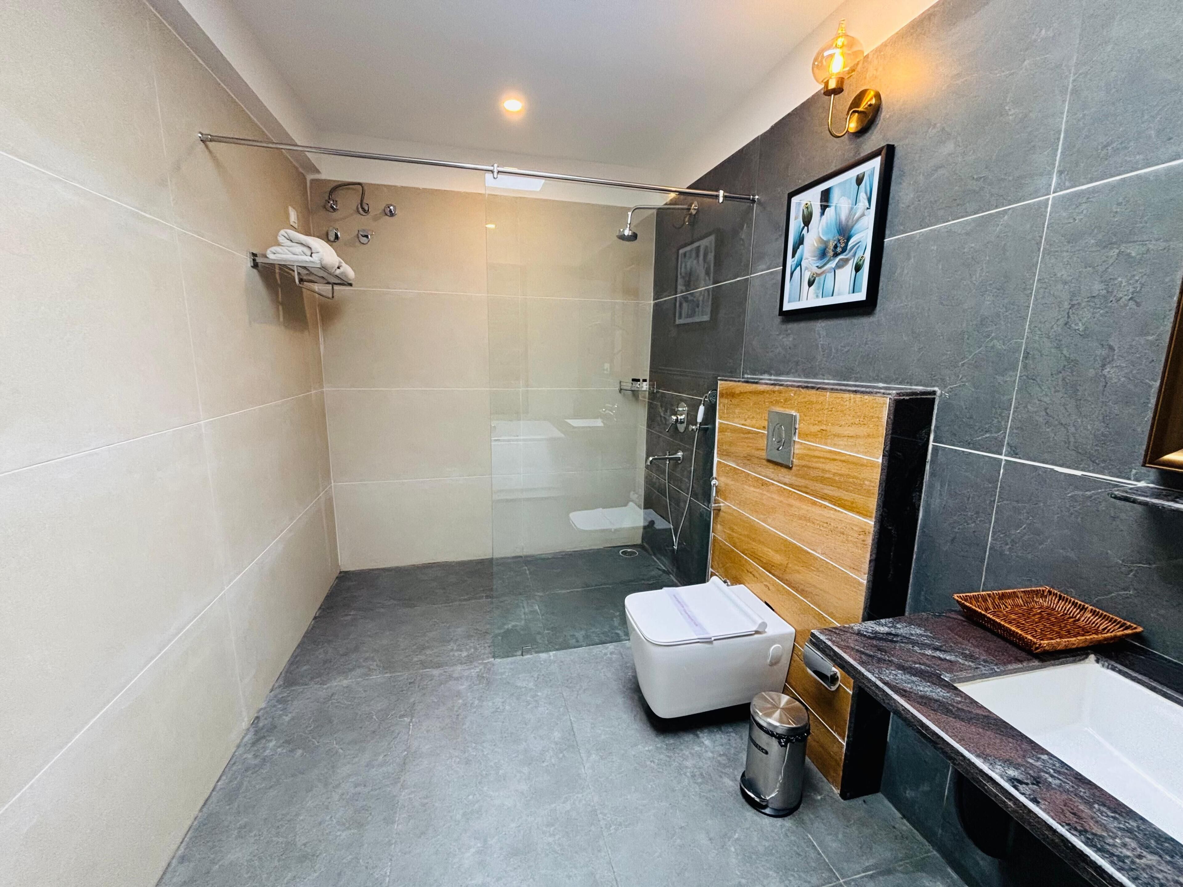 Un baño moderno con ducha envuelta en vidrio, inodoro blanco, tocador de madera con lavabo y un cubo de basura.