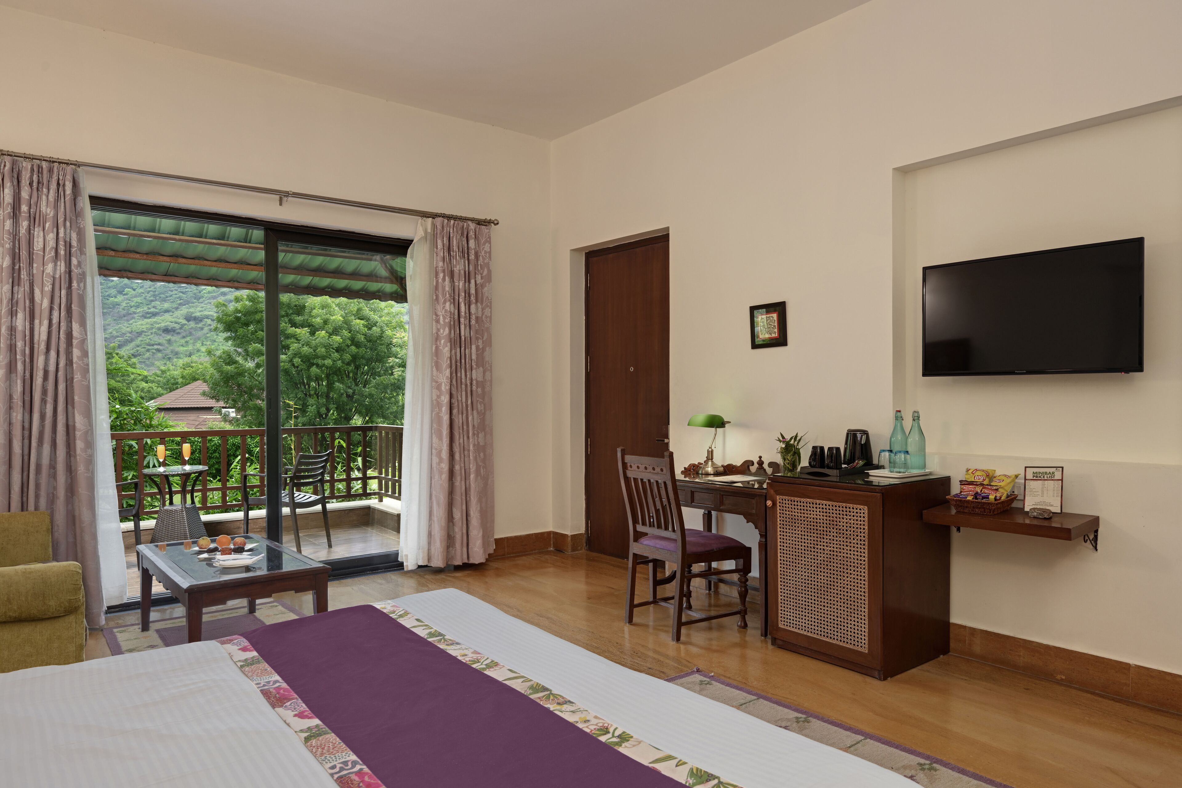 Une chambre d’hôtel comprenant un lit, un bureau, une chaise, une télévision et un balcon avec une table et des chaises.