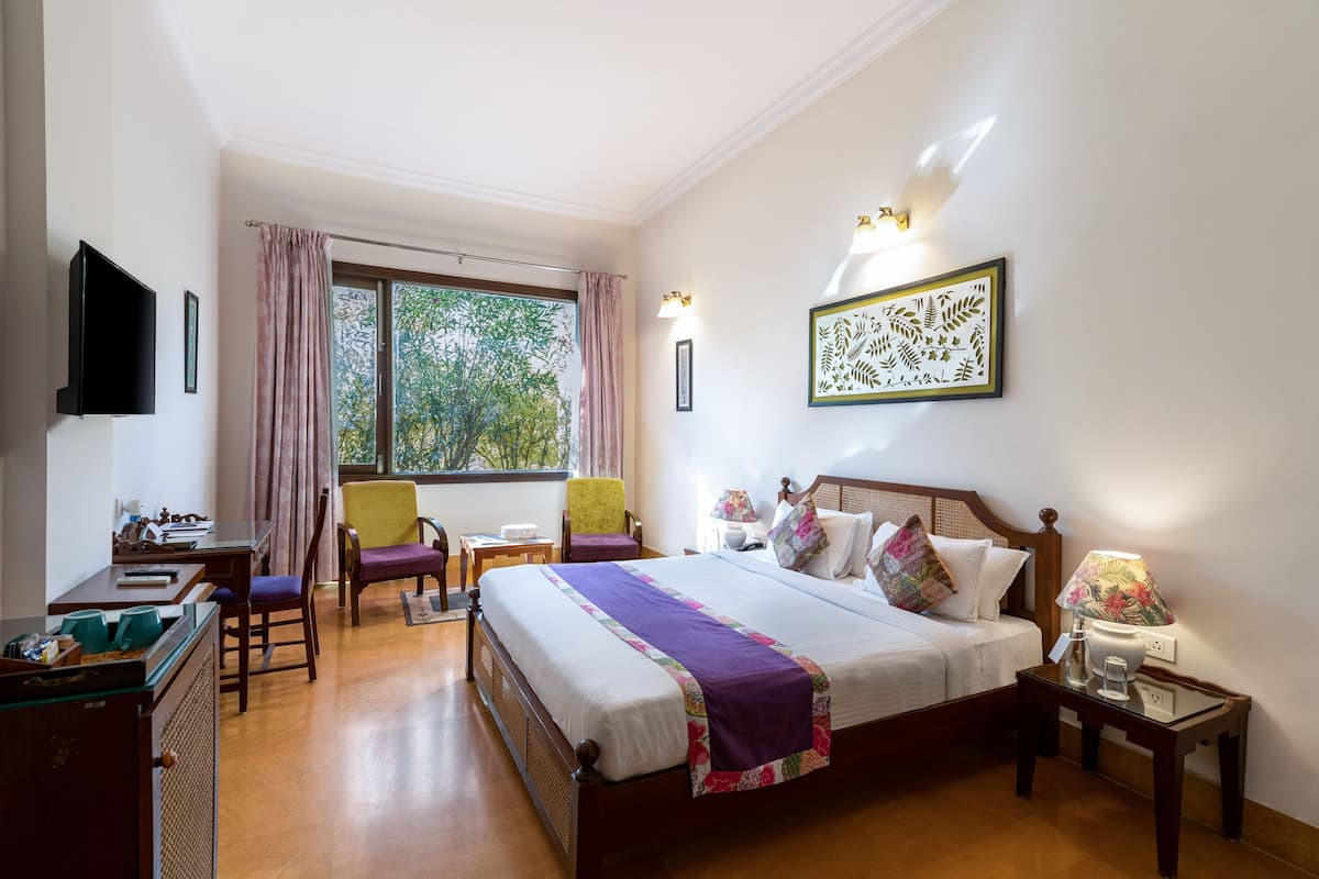 A hotel room with a bed, a desk, a chair, a TV, and a window with curtains.