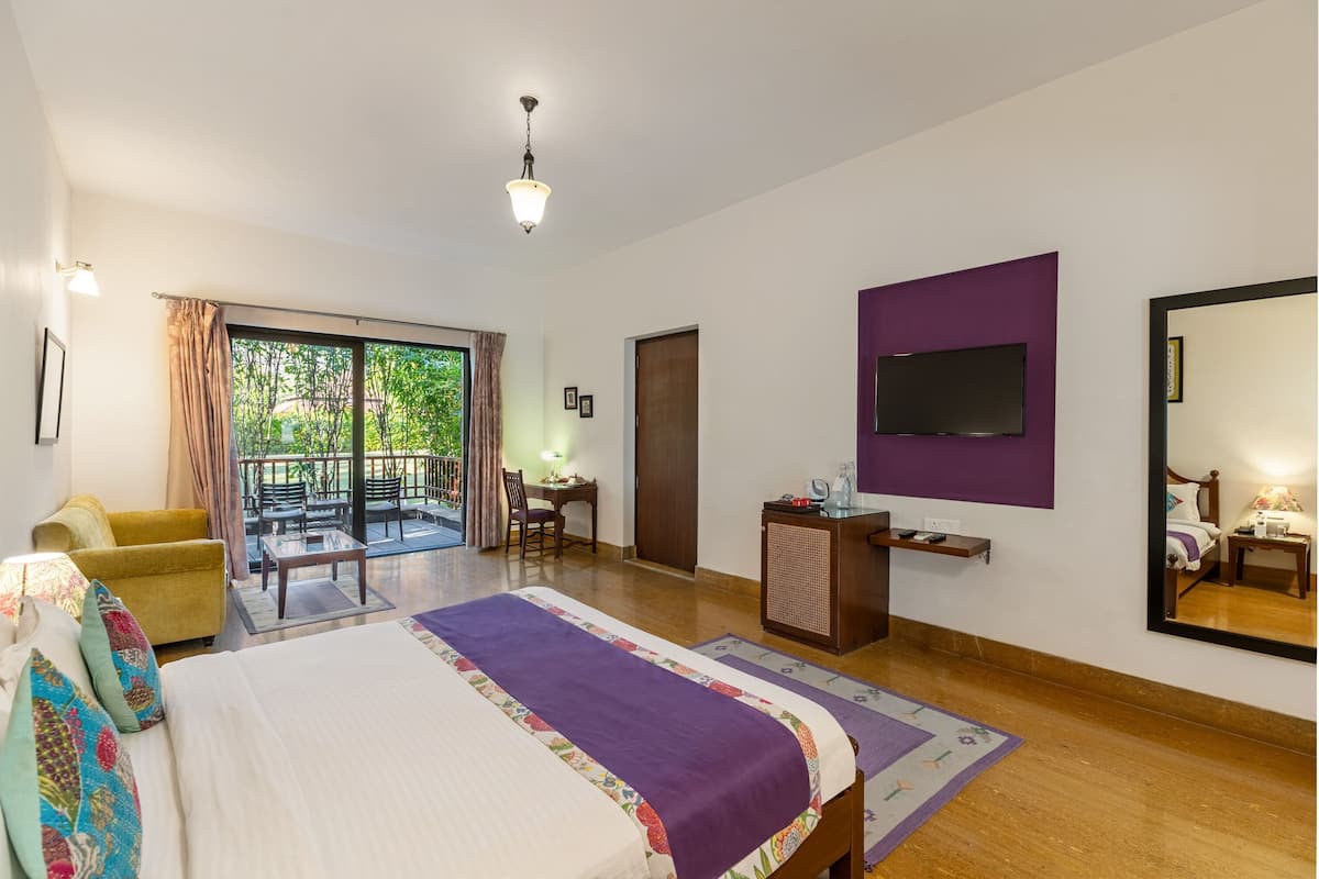 A hotel room with a bed, a desk, a chair, a TV, and a balcony with a view of greenery.