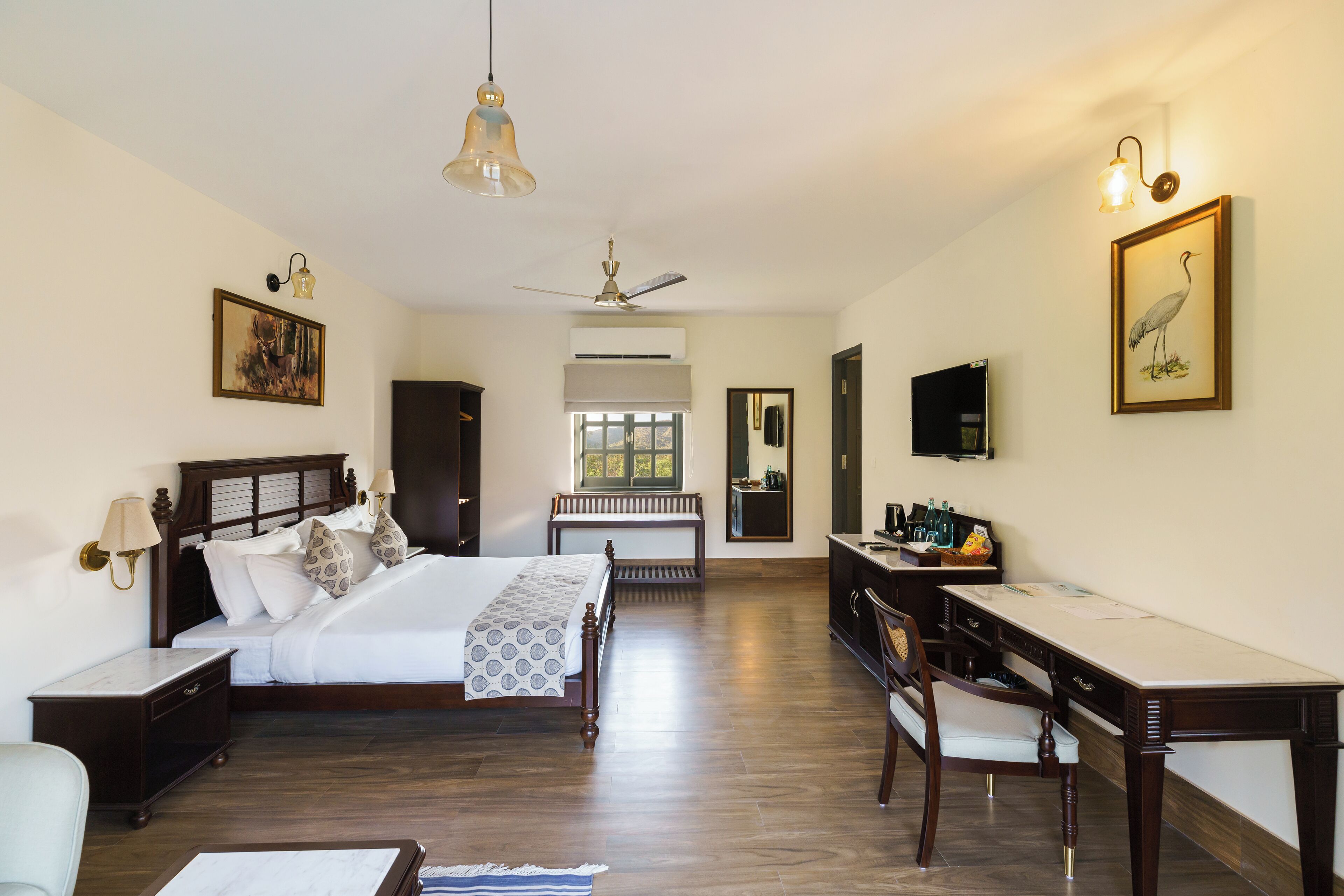 Quarto de hotel com cama, escrivaninha, cadeira e televisão.