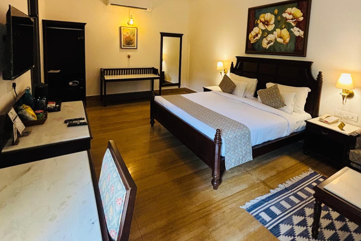 A hotel room with a large bed, a desk, a chair, a television, and a painting on the wall.