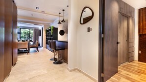 Een modern interieur met een houten vloer, een zithoek met tafel en stoelen, een keuken met barkrukken, en een grote spiegel aan de muur.