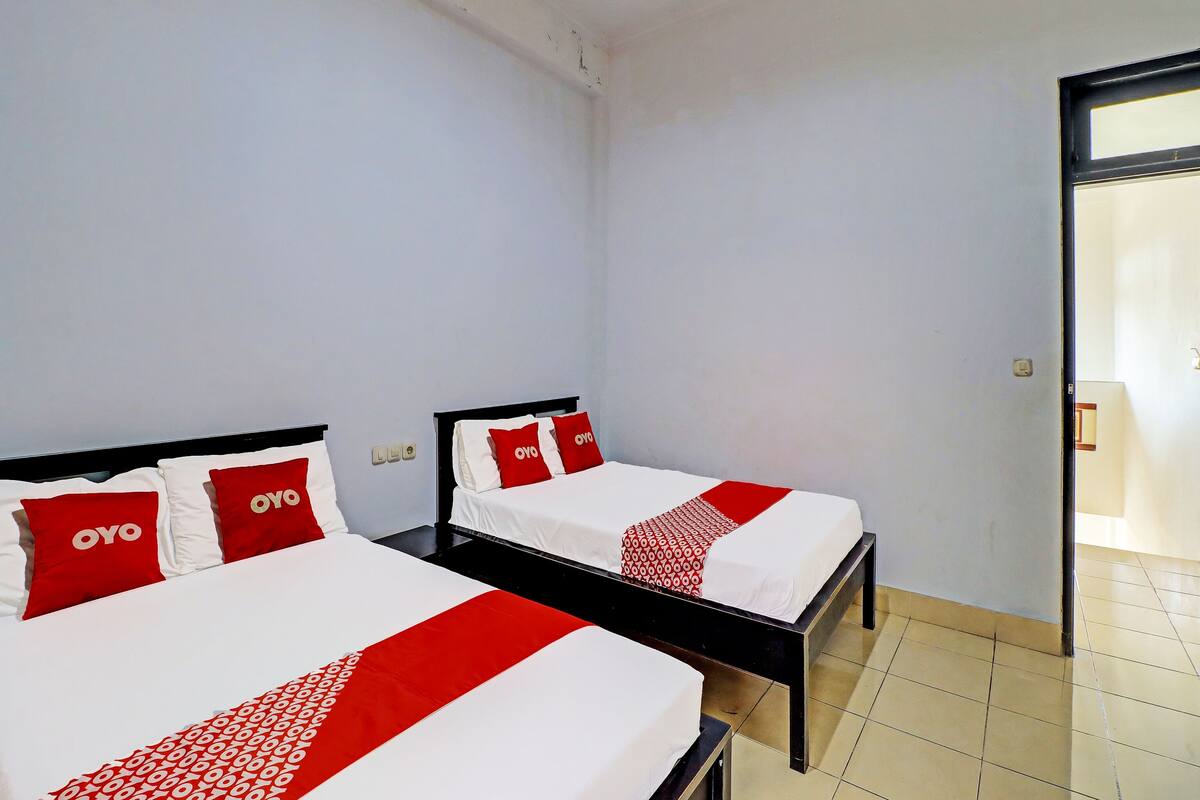 Une chambre d’hôtel avec deux lits, chacun agrémenté de linge de lit blanc et de touches de couleur rouge, et un sol carrelé.