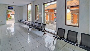 Une salle d’attente avec des rangées de chaises, de grandes fenêtres et un écran de télévision.
