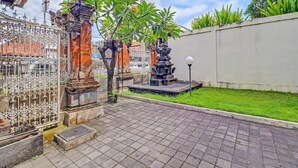 Une cour avec un sol carrelé, une clôture décorative, un petit arbre et une statue.