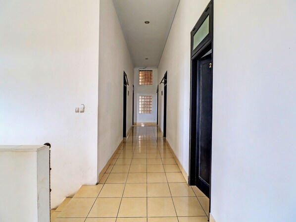 A corridor with tiled flooring, white walls, and a door with a number plate.
