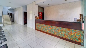 Un hall d’hôtel avec un sol carrelé, un escalier, un comptoir d’accueil doté d’un socle en mosaïque colorée et un réfrigérateur Coca-Cola.