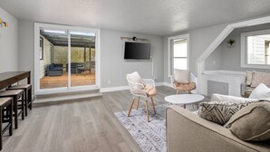 A spacious living area with a large sliding glass door leading to an outdoor patio, a flat-screen TV mounted on the wall, and a cozy seating arrangement with a sofa and two chairs. - Spectacular Single Level Estate, Pet Friendly, Huge Fully Fenced Backyard, Covered Patio, Game Room (Portland)
