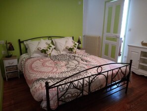 A bed with a patterned bedspread, a nightstand with a lamp, and a radiator in a room with green walls and a wooden floor. - My house by the water (Villefranche-de-Rouergue)