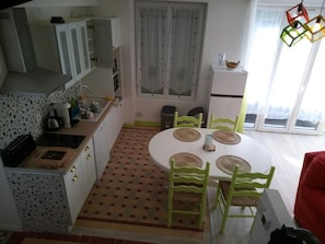 A compact kitchen with a dining area, featuring a round table with woven placemats, green chairs, and a white cabinet.