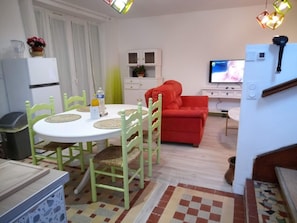 A compact living space with a dining area, a red sofa, a television, and a kitchen area.