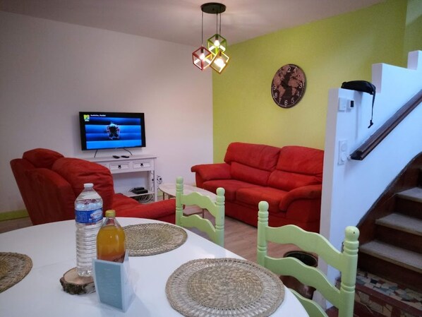 A living room with a TV, red sofas, a staircase, and a dining table with placemats.