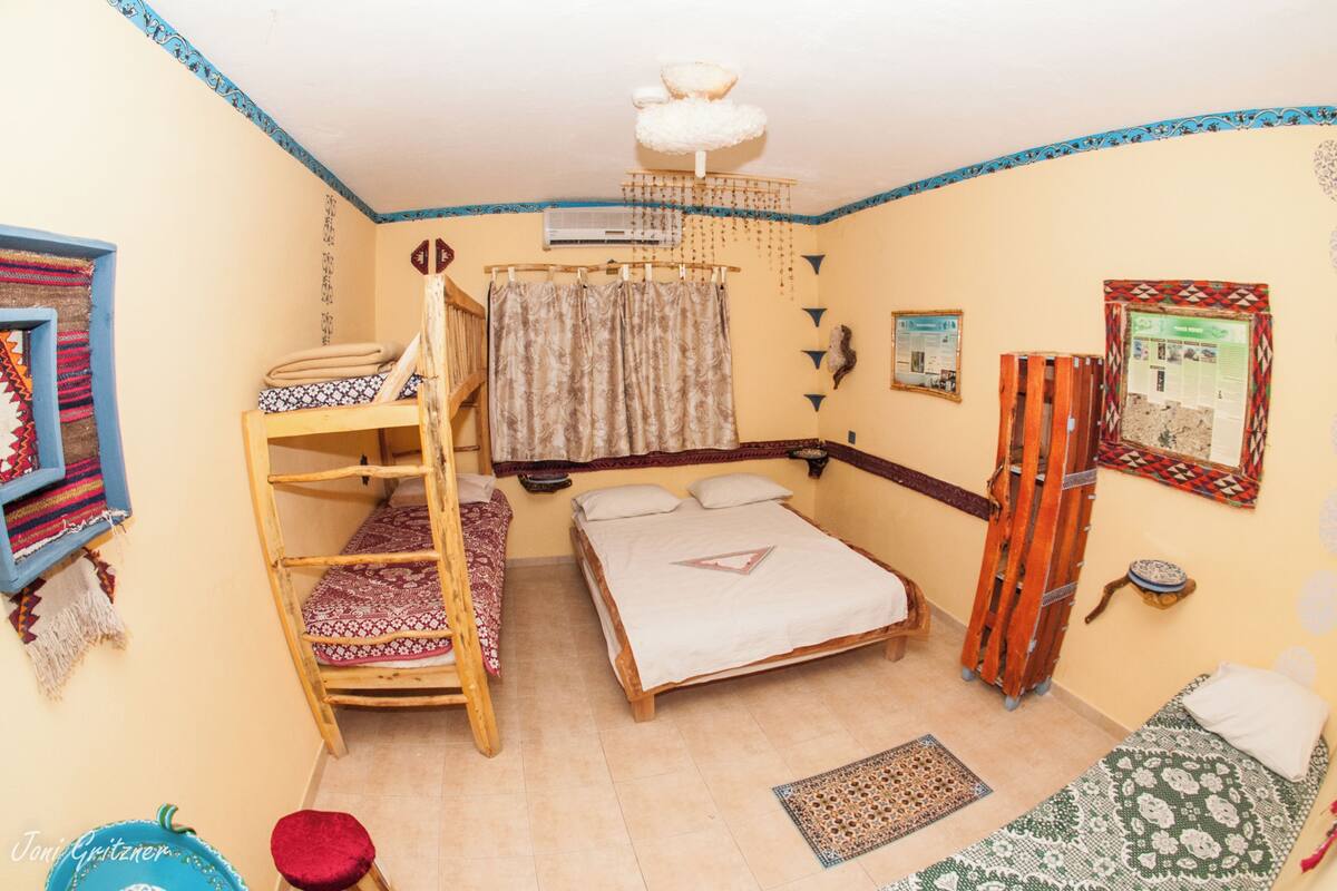A room with a bunk bed, a single bed, a wooden ladder, a hanging curtain, and a ceiling fan.