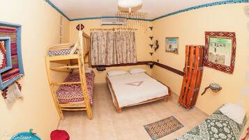 Una habitación con una cama litera, una cama individual, una escalera de madera, una cortina colgante y un ventilador de techo.