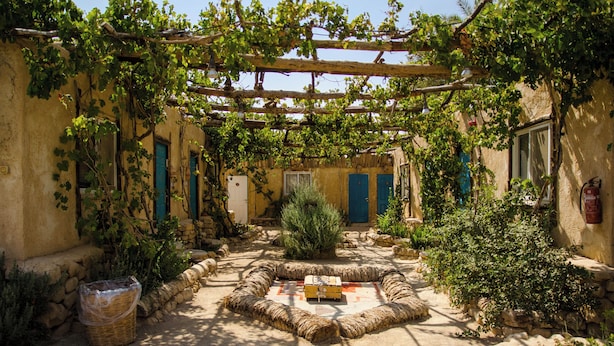 En innergård med en central sittgrupp, stenmurar och en pergola som är täckt av klätterväxter.