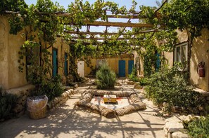 A courtyard with a central seating area, stone walls, and a pergola covered in vines. - Kfar Hanokdim A GREEN ISLAND IN THE DESERT (Tamar)