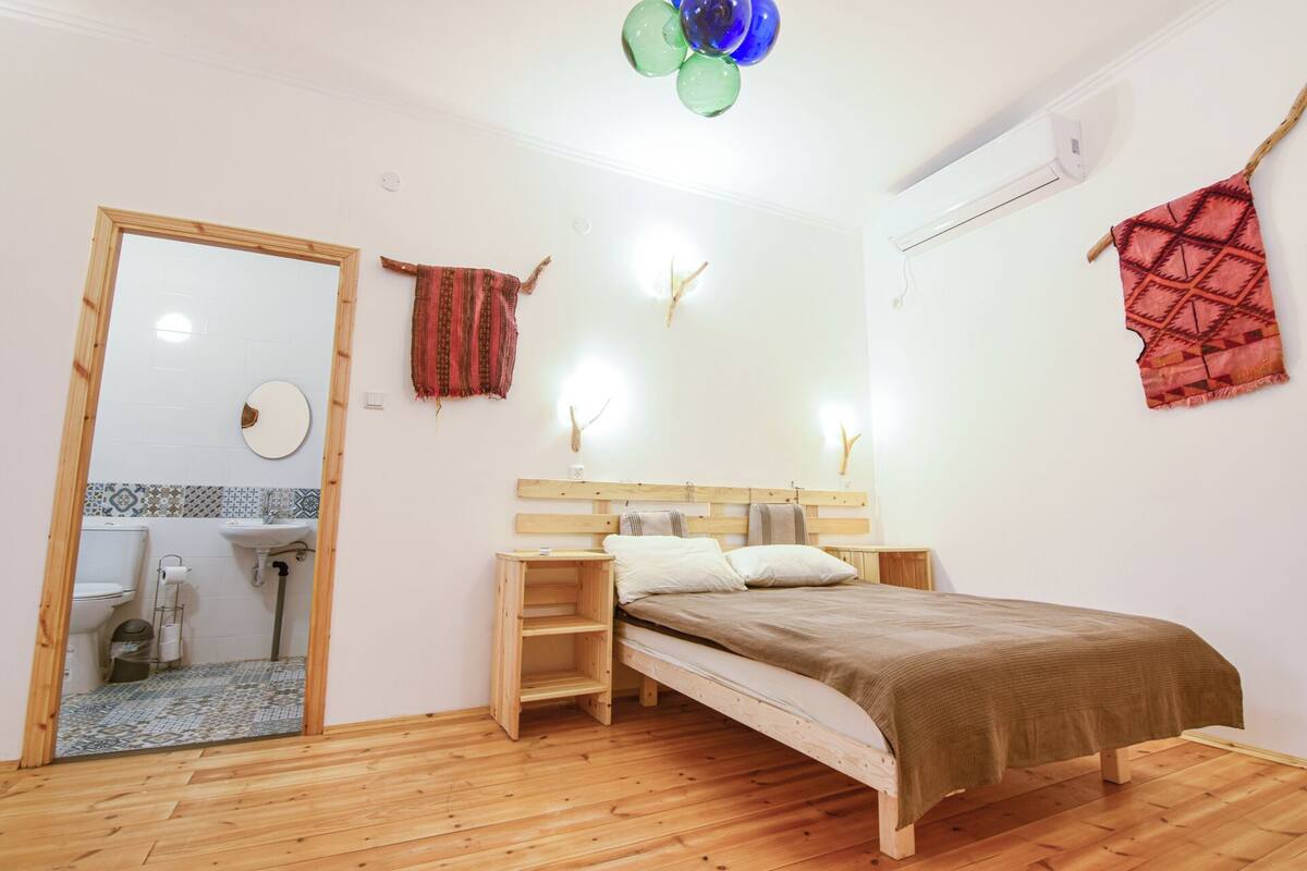 A bedroom with a wooden bed, a wooden desk, a mirror, and a bathroom visible through an open door.