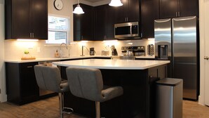 Una cocina moderna con armarios oscuros, electrodomésticos de acero inoxidable, una isla grande con taburetes de bar e iluminación colgante.