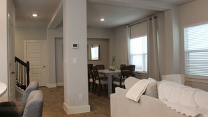 Una sala de estar con un sofá, una mesa de comedor con sillas y una escalera que lleva a otra habitación.