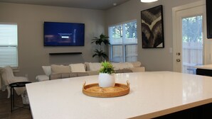Una cocina moderna con una isla central, un televisor de pantalla plana montado en la pared y un gran ventanal con persianas.