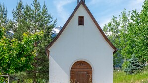 Una iglesia blanca pequeña con un campanario, rodeada de pastos altos y árboles.