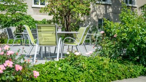 Un área de estar al aire libre con una mesa y sillas, rodeada de abundante vegetación y plantas con flores.