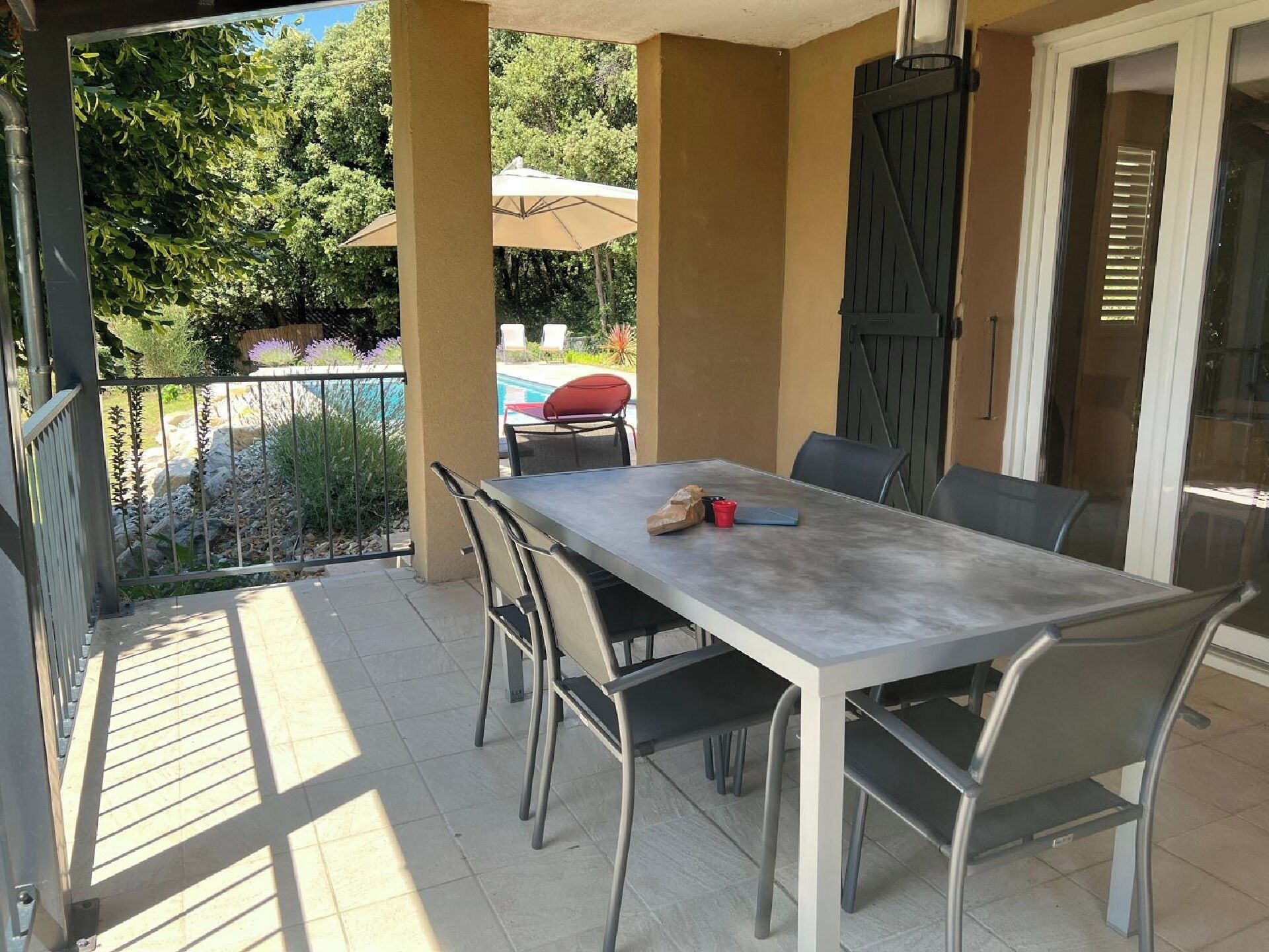 Une terrasse avec une table et des chaises, une piscine et un espace abrité avec des parasols.