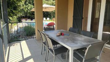 Une terrasse avec une table et des chaises, une piscine et un espace abrité avec des parasols.