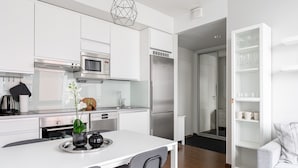 Une cuisine moderne avec des meubles blancs, un réfrigérateur en acier inoxydable et un coin repas comprenant une table et des chaises blanches.