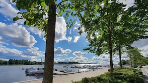 Un port de plaisance au bord d’un lac, avec des bateaux amarrés, entouré d’arbres et sous un ciel dégagé.