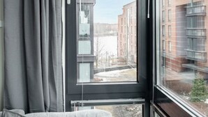 Une pièce avec une grande fenêtre, des rideaux gris et un lit avec une literie grise.